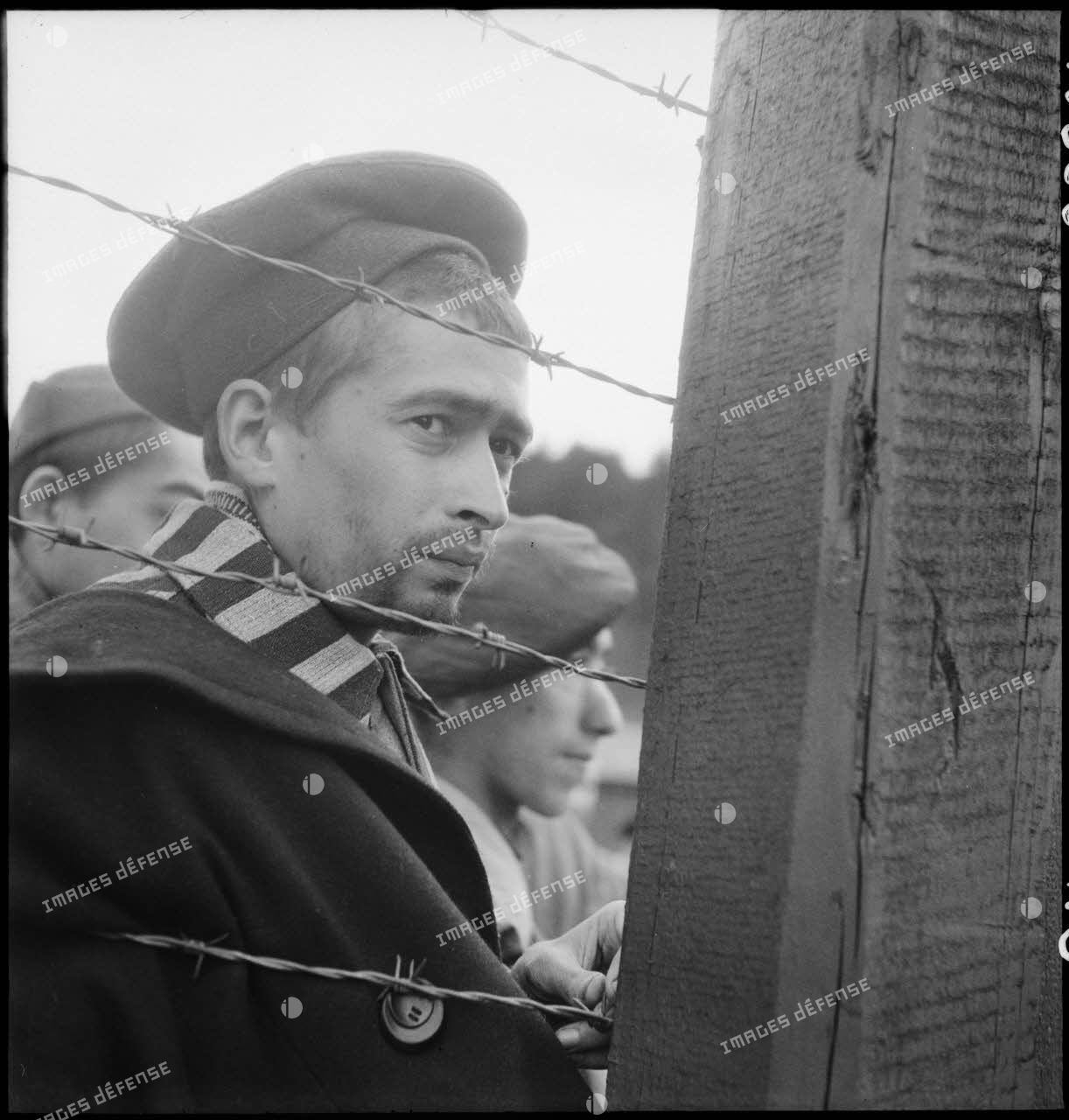 Portrait d'un déporté derrière des barbelés du camp de Vaihingen récemment libéré par des troupes françaises.