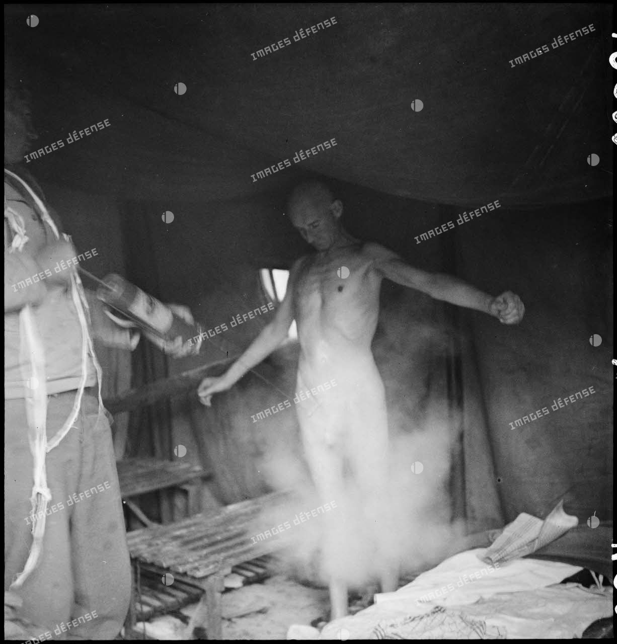 Un personnel d'un bataillon médical pulvérise du produit désinfectant sur un déporté du camp de Vaihingen libéré.