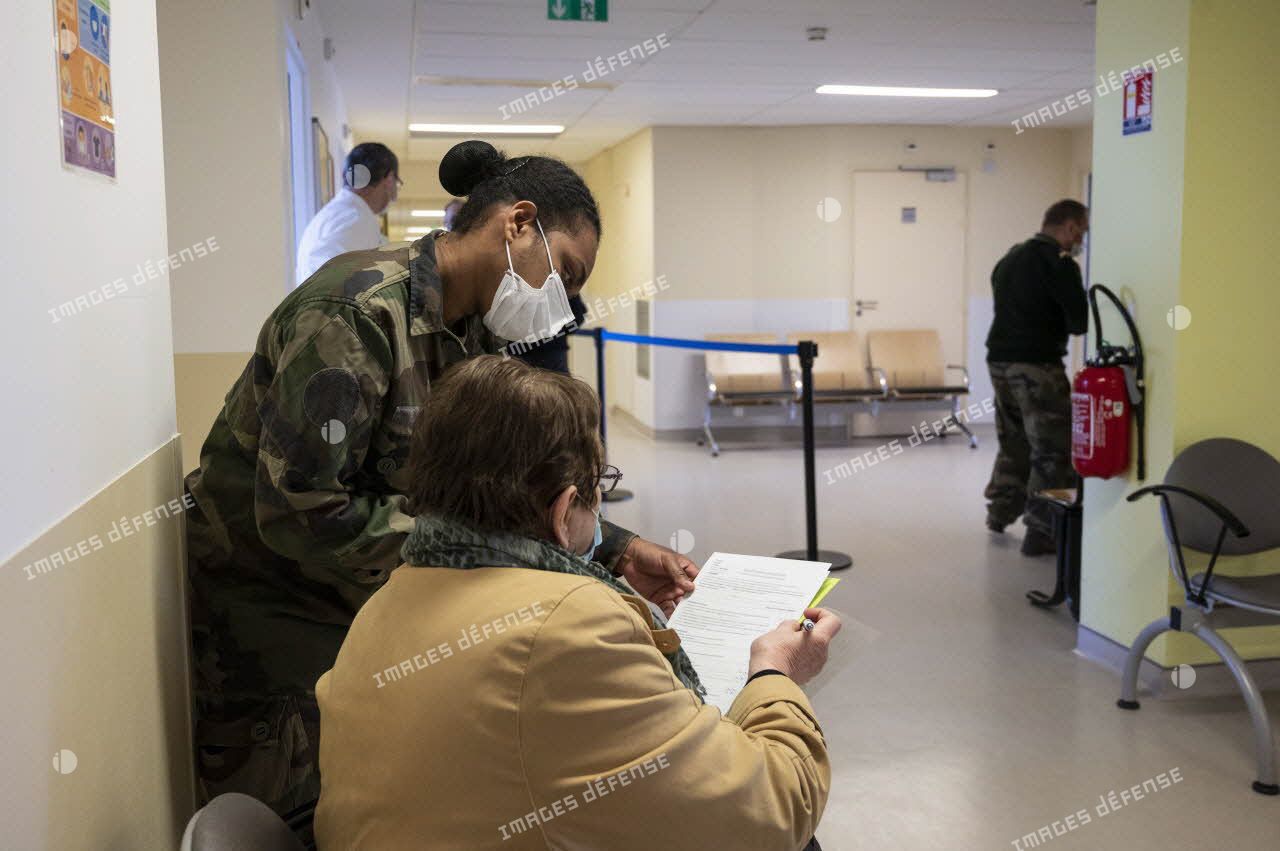 Un militaire aide une patiente à remplir son formulaire de vaccination au sein de l'hôpital d'instruction des armées (HIA) Bégin.