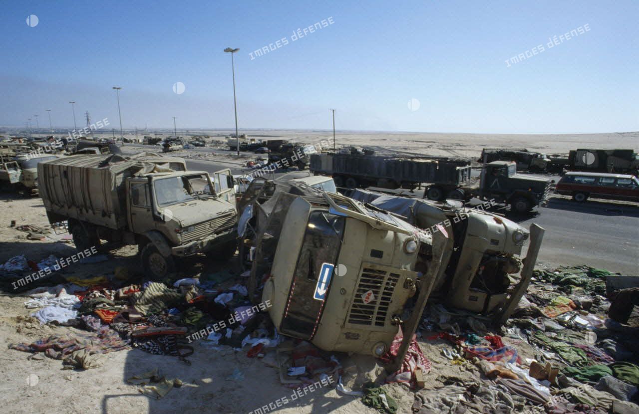 Carcasses de véhicules détruits et abandonnés à la sortie de Koweit City, dont des camions Gaz-66 4x4. Des tissus jonchent le sol.