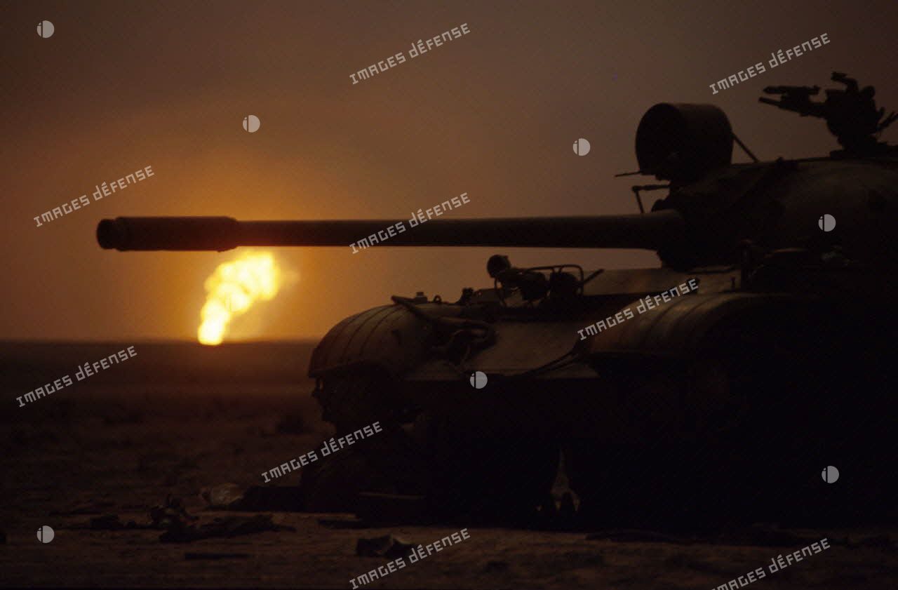 Les puits de pétrole en feu aux environs de Koweit city derrière un char irakien T-55 détruit.