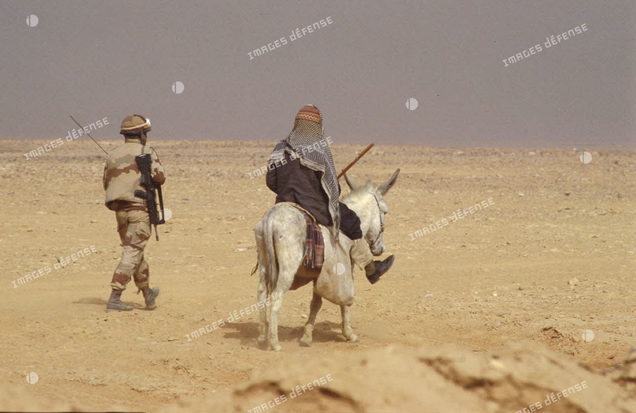Une sentinelle française accompagne Un bédouin qui chevauche un âne aux abords du PC (poste de commandement) divisionnaire.