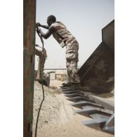 Une sapeur du 19e régiment du génie (RG) arrime un container à une chargeuse pelleteuse 821C pour son transport sur la base de Tombouctou, au Mali.