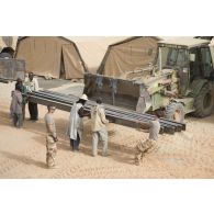 Des sapeurs du 19e régiment du génie (RG) aidés par des ouvriers civils déchargent du matériel pour la consolidation de l'enceinte de la base de Tombouctou, au Mali.