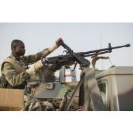 Un soldat nigérien entretient une mitrailleuse lourde Norinco QJC-88 de 12,7 mm à bord d'un pick-up lors de la halte d'un convoi dans la région d'Ayorou, au Niger.