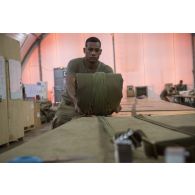 Le soldat de 1re classe Romain du 1er régiment du train parachutiste (RTP) roule la voilure et les suspentes d'un parachute pour son pliage à Niamey, au Niger.