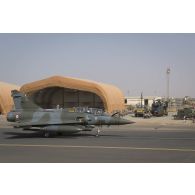 Passage d'un avion Mirage 2000 D devant un hangar abritant la maintenance opérationnelle d'un hélicoptère Caïman NH-90 TTH sur la base aérienne de Niamey, au Niger.