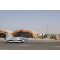 Passage d'un avion Mirage 2000 C devant un hangar abritant la maintenance opérationnelle d'un hélicoptère Caïman NH-90 TTH sur la base aérienne de Niamey, au Niger.