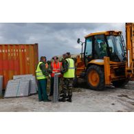 Des militaires du 25e RGA se concertent avant l'assemblage d'éléments de structure pour l'édification de gabions à proximité d'un container, et à côté d'une tractopelle grecque JCB 3CB.