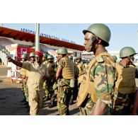 Rassemblement devant l'aérogare de l'aéroport de Bamako de militaires togolais fraîchement débarqués, et consignes d'un commandant burkinabé.