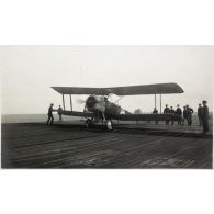 Mars 1920. Escadre anglaise à Alger. Le pont supérieur de l'"Argus", bateau porte-avions. L'avion atterrit : des pinces, plusieurs en-dessous de l'appareil, agrippent les cables en fer tendus parallèlement sur les planches et forment frein. [légende d'origine]