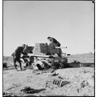 Deux soldats français examinent l'épave d'un canon automoteur Semovente L40 47/32 de l'armée italienne dans le désert tunisien.