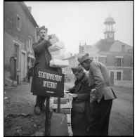 Photographie de groupe de soldats de la 55e DI qui portent des paquets dans une rue.
