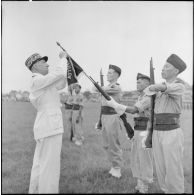 Le général Marchand, adjoint du commandant de la zone opérationnelle du Tonkin, décore le fanion du bataillon de marche indochinois (BMI) de la Croix de guerre avec palme au cours d'une cérémonie sur le stade d'Haïduong.