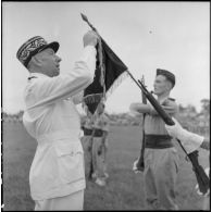 Le général Marchand, adjoint du commandant de la zone opérationnelle du Tonkin, décore le fanion du bataillon de marche indochinois (BMI) de la Croix de guerre avec palme au cours d'une cérémonie sur le stade d'Haïduong.