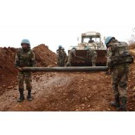 Les sapeurs du 13e RG (régiment du Génie) transportent une roquette non explosée en vue de sa destruction vers la benne d'une pelleteuse.