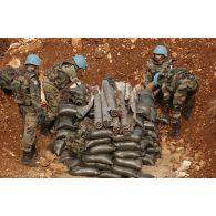 Mise en place par les sapeurs du 13e RG (régiment du Génie) de pains de plastic et des fils détonateurs en couches successives d'explosifs et de munitions et de sous-munitions dans le fourneau, en vue de leur destruction. Le fourneau, surmonté de roquettes non explosées, est entouré de sacs-à-terre.