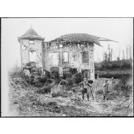 [Un opérateur de cinéma britannique et son assistant devant une maison en ruines.]