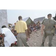 Jeunes enfants regroupés, surveillés et soignés avec l'aide de personnels militaires et de civils dans un camp de réfugiés.