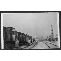 [Soldats réunis devant des wagons dans une gare].