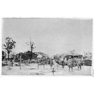[Soldats dans un cimetière devant des maisons en ruine].