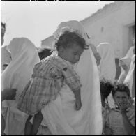 Portrait d'une femme qui tient son enfant dans ses bras pendant l'intervention d'une équipe médico-sociale itinérante (EMSI), dans un douar d'Oran.