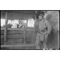 [Un soldat fume la pipe devant une grange].