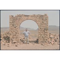 Un officier du DMAT d'Atar pose sous l'arche des ruines du décor de cinéma réalisé pour le film "Fort Saganne". [légende d'origine]