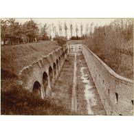 Les fossés. Au fond une caponnière où des canons revolvers sont en batterie pour mitrailler les ennemis descendus dans les fossés en cas d'assaut. [légende d'origine]