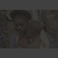 Portrait d'un homme âgé tenant dans ses bras un enfant en pleurs portant des cicatrices sur la nuque et un vêtement tâché au camp de réfugiés de Kibeho.