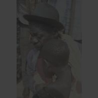 Portrait d'un homme âgé tenant dans ses bras un enfant en pleurs portant des cicatrices sur la nuque et un vêtement tâché à Kibeho.