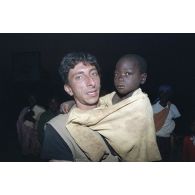 Charles Caratini, photographe de l'agence Sygma, porte un enfant dans les bras au campement de l'élément militaire médical d'intervention rapide (EMMIR) à Cyangugu lors d'une évacuation de blessés.