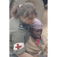 Un militaire féminin de l'élément militaire médical d'intervention rapide (EMMIR) soutient une jeune femme lors de son examen médical au camp de réfugiés de Kibeho en vue d'une évacuation sanitaire.