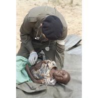 Un médecin principal de l'élément militaire médical d'intervention rapide (EMMIR) ausculte un enfant sur une bâche étalée au sol au camp de réfugiés de Kibeho en vue de son évacuation sanitaire.