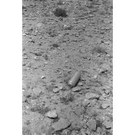 Gros plan sur un objet métallique, peut-être une munition, posée sur le sol.