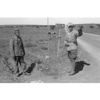 Un soldat et un Oberleutnant posent près de deux panneaux indiquant la localisation d'unités de la 21-Pz.Div.