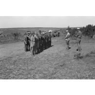 Un lieutenant (Oberleutnant) parle à ses hommes en rang. En arrière plan un camion Opel Blitz chargé de caisses.