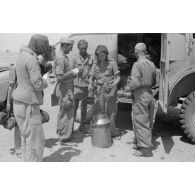 Soldats remplissent leur gourde devant un camion britannique de prise, le code postale FP 17967 est peint sur le véhicule.