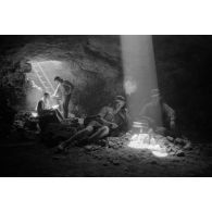 Deux soldats utilisent un téléphone de campagne à l'intérieur d'une grotte où filtre un rayon de lumière.