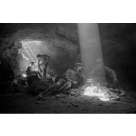 Deux soldats utilisent un téléphone de campagne à l'intérieur d'une grotte où filtre un rayon de lumière.