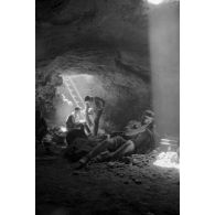 Deux soldats utilisent un téléphone de campagne à l'intérieur d'une grotte où filtre un rayon de lumière.