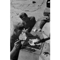 Un homme d'équipage casse des oeufs sur la plaque d'un casier extérieur du Panzer II et les fait cuire.
