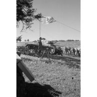 L'officier près de l'autel. Au premier plan, un faisceau de fusils, en arrière-plan, le drapeau national allemand et un char Panzer III.