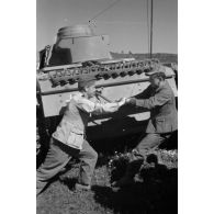 A l'issue d'une prise d'armes, deux soldats font démarrer le moteur du Panzer III à l'aide d'une manivelle.