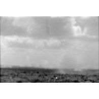 Le groupe d'officiers observe à la jumelle les combats. Impacts d'artillerie dans le désert (image floue).