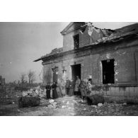 [Un groupe de soldats pose à côté de civils devant une mairie-école en ruines, s.d.]