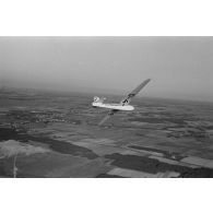 Un planeur monoplace de type DFS Habicht, du N.S.F.K. (Nationalistischen Flieger-Korps) en vol au dessus d'un paysage agricole allemand.