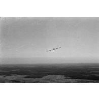 Un planeur monoplace de type DFS Habicht, du N.S.F.K. (Nationalistischen Flieger-Korps) en vol au dessus d'un paysage agricole allemand.