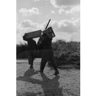 Des servants d'une pièce de Flak calibre 8,8 cm Flak 18-L56, dans un poste en bois, apportent des caissons de munitions, sur leur dos.