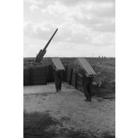 Des servants d'une pièce de Flak calibre 8,8 cm Flak 18-L56, dans un poste en bois, apportent des caissons de munitions, sur leur dos.